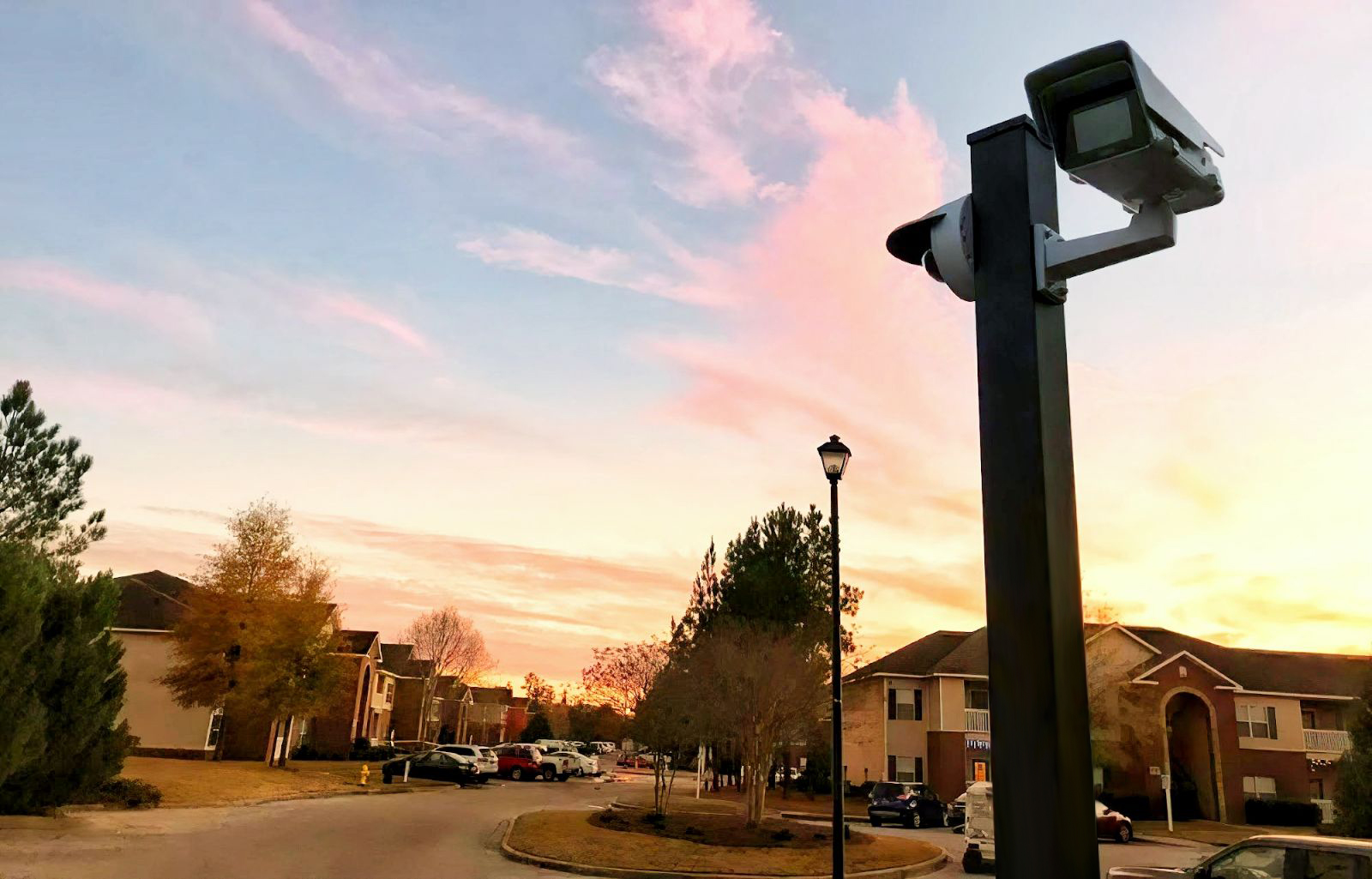 A security camera mounted on a multifamily property silhouetted against a vibrant sunset sky.