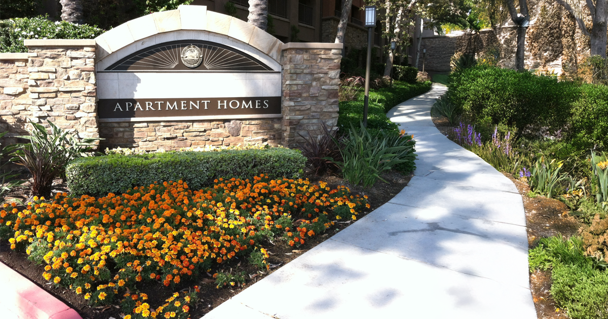 A welcoming apartment community sign surrounded by blooming spring flowers and lush green grass, representing the renewal and activity of the season.